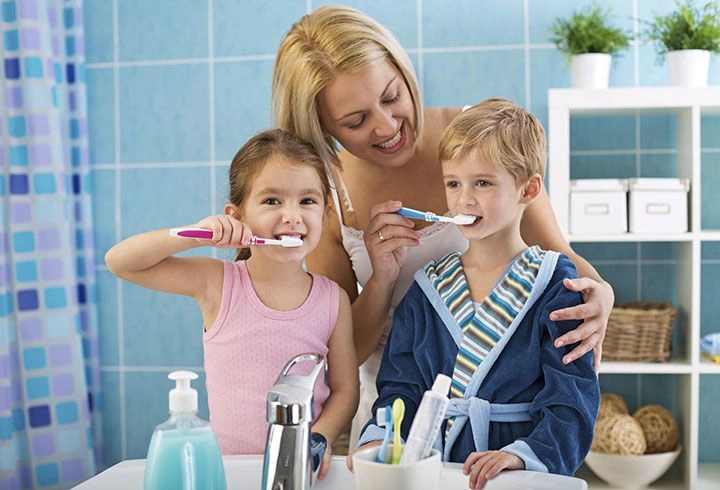 Mother teaching kids proper brushing habits, supported by the best dental clinics in Kasaragod for healthy smiles.